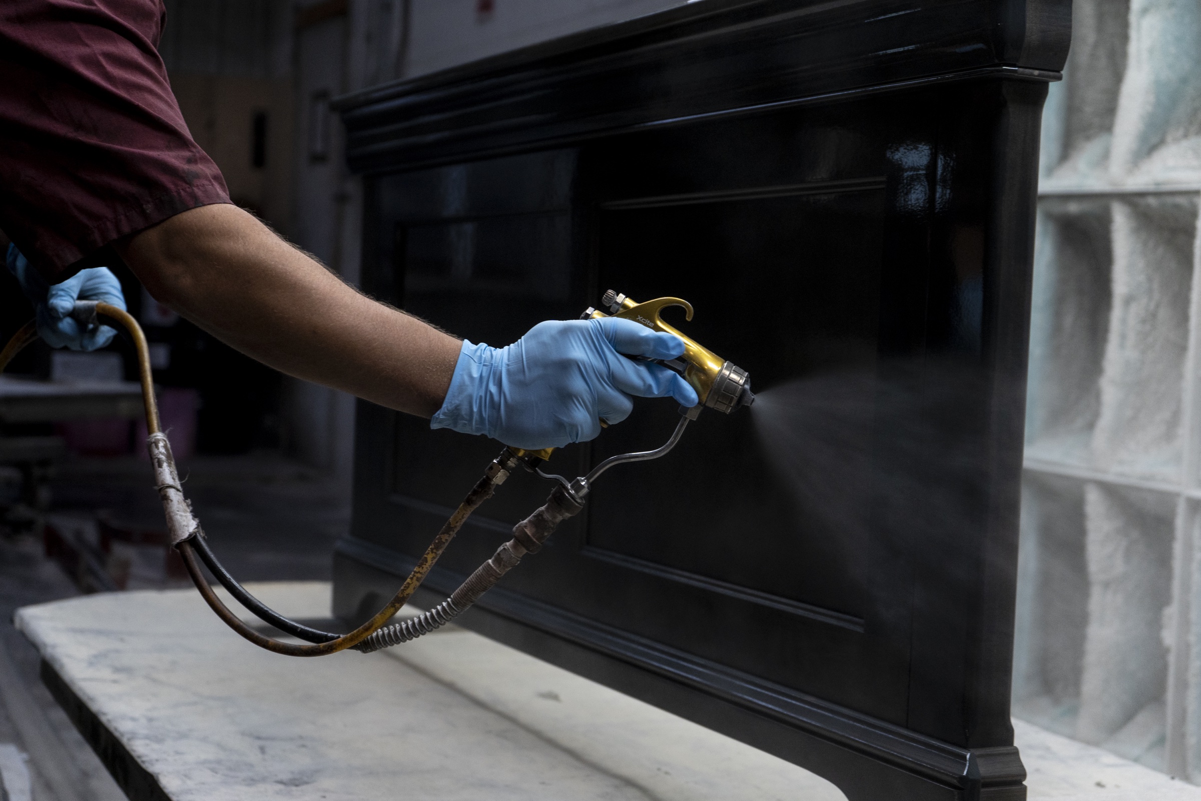 Craftsperson applying a dark wood finish with a spray tool